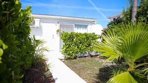 A white house with a small garden, a palm tree, and a clear blue sky. - Tangerine Sunsets Seville (Nassau)