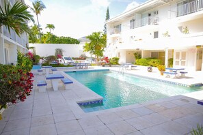 A swimming pool with lounge chairs and a white building with balconies. - Tangerine Sunsets Seville (Nassau)