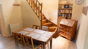 A dining area with a wooden table and chairs, a staircase, a bookshelf, and a radiator. - Cottage - Peaceful and nature (Cieux)