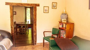 A cozy living room with a wooden door leading to a dining area, a green sofa, and a bookshelf with books and a decorative vase. - Cottage - Peaceful and nature (Cieux)