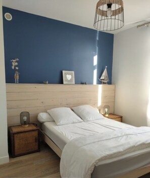 A bedroom with a wooden headboard, a bed with white bedding, two bedside tables with lamps, and a wall-mounted shelf with decorative items.