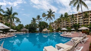 A swimming pool surrounded by lounge chairs and umbrellas, with palm trees and a hotel building in the background. - Beautiful Studio with balcony inside resort (Puerto Vallarta)