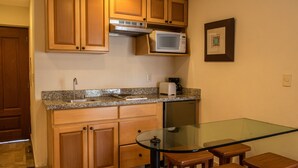 A compact kitchen with wooden cabinets, a microwave, a toaster, and a glass-top table with stools. - Beautiful Studio with balcony inside resort (Puerto Vallarta)