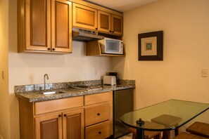 A compact kitchen with wooden cabinets, a microwave, a toaster, and a glass table.