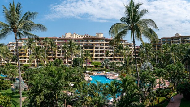 A hotel with multiple balconies, a swimming pool, and lush palm trees. - Beautiful Studio with balcony inside resort (Puerto Vallarta)