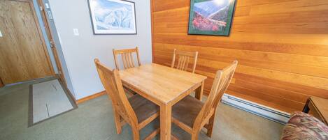 A wooden-paneled room with a dining table and chairs, two framed pictures on the wall, and a carpeted floor.