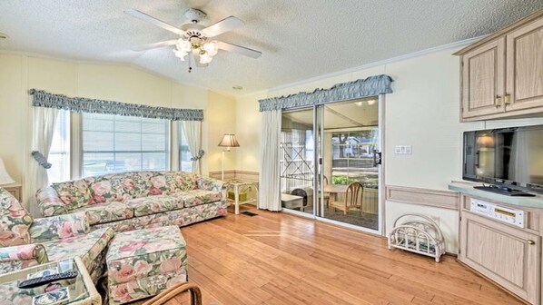 A living room with a floral sofa, wooden flooring, a ceiling fan, and a sliding glass door leading to a balcony. - Relaxing Home Pool Access and Screened-In Porch! (Sarasota)