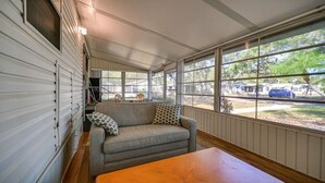 A cozy room with a sofa, a wooden table, and large windows offering a view of the outside. - Relaxing Home Pool Access and Screened-In Porch! (Sarasota)