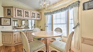 A dining area with a round table and four chairs, a kitchen with light wood cabinets, and a chandelier. - Relaxing Home Pool Access and Screened-In Porch! (Sarasota)