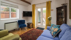 A living room with a blue sofa, a green armchair, a red patterned rug, a television, and a wooden cabinet. - Mirrored Reflections (London)