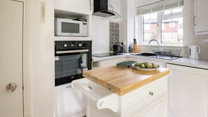 A compact kitchen with white cabinetry, a microwave, an oven, a coffee maker, and a sink. - Mirrored Reflections (London)