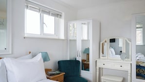 A bedroom with a bed, a desk with a mirror, a chair, and a window with blinds. - Mirrored Reflections (London)