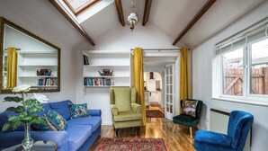 A living room with a blue sofa, a green armchair, a blue armchair, a red patterned rug, and a glass coffee table. - Mirrored Reflections (London)
