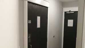 Een gang met twee zwarte deuren, elk met een bordje erop. De gang heeft een houten vloer en witte wanden.