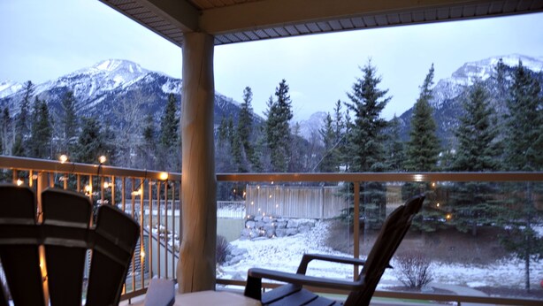 Een balkon met stoelen en een tafel, met uitzicht op een besneeerd landschap met bomen en bergen.