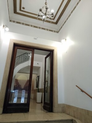A grand staircase with a wooden handrail, a glass door with a decorative frame, and a chandelier. - Enjoy our warm open apartment in a historical building. (CABA)
