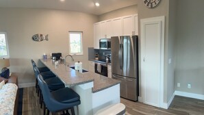 A modern kitchen with a central island, stainless steel appliances, and a clock on the wall. - Coconut Castaway | Ocean Views, Golf Cart & Club Pool (Upper Captiva)