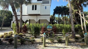 A two-story building with a balcony, surrounded by palm trees and a rope barrier. - Coconut Castaway | Ocean Views, Golf Cart & Club Pool (Upper Captiva)