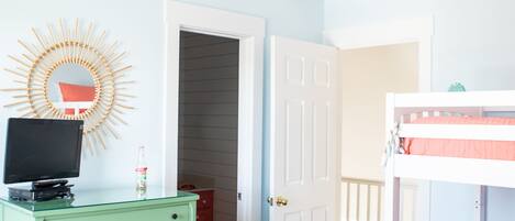A bedroom with a bed, a dresser, a ceiling fan, and a door leading to another room.