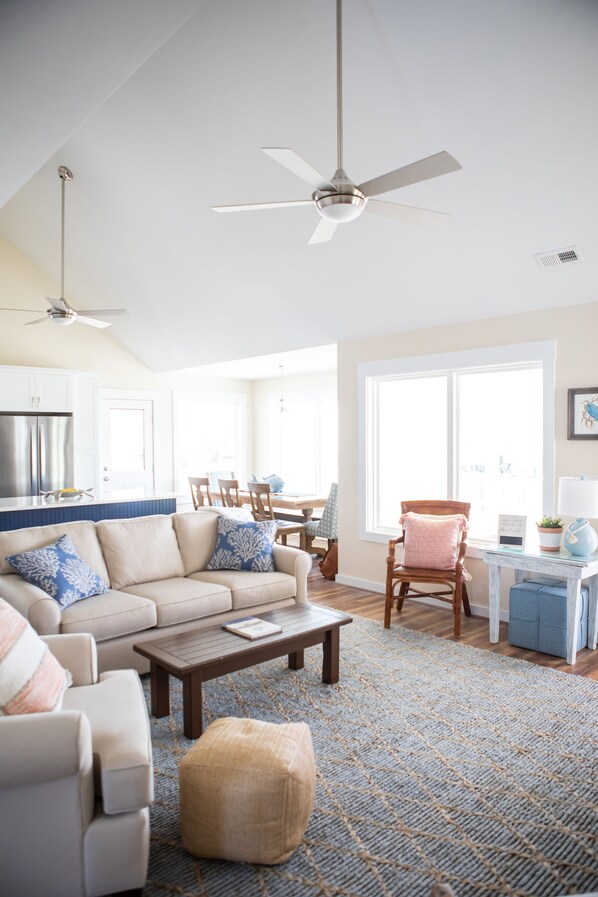 A spacious living room with a sofa, coffee table, and a dining area in the background. - PERFECT LOCATION, 2nd row home with beach access across the street! (Ocean Isle Beach)