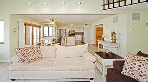 A living room with a sofa, a coffee table, and a dining table. There is a kitchen in the background.