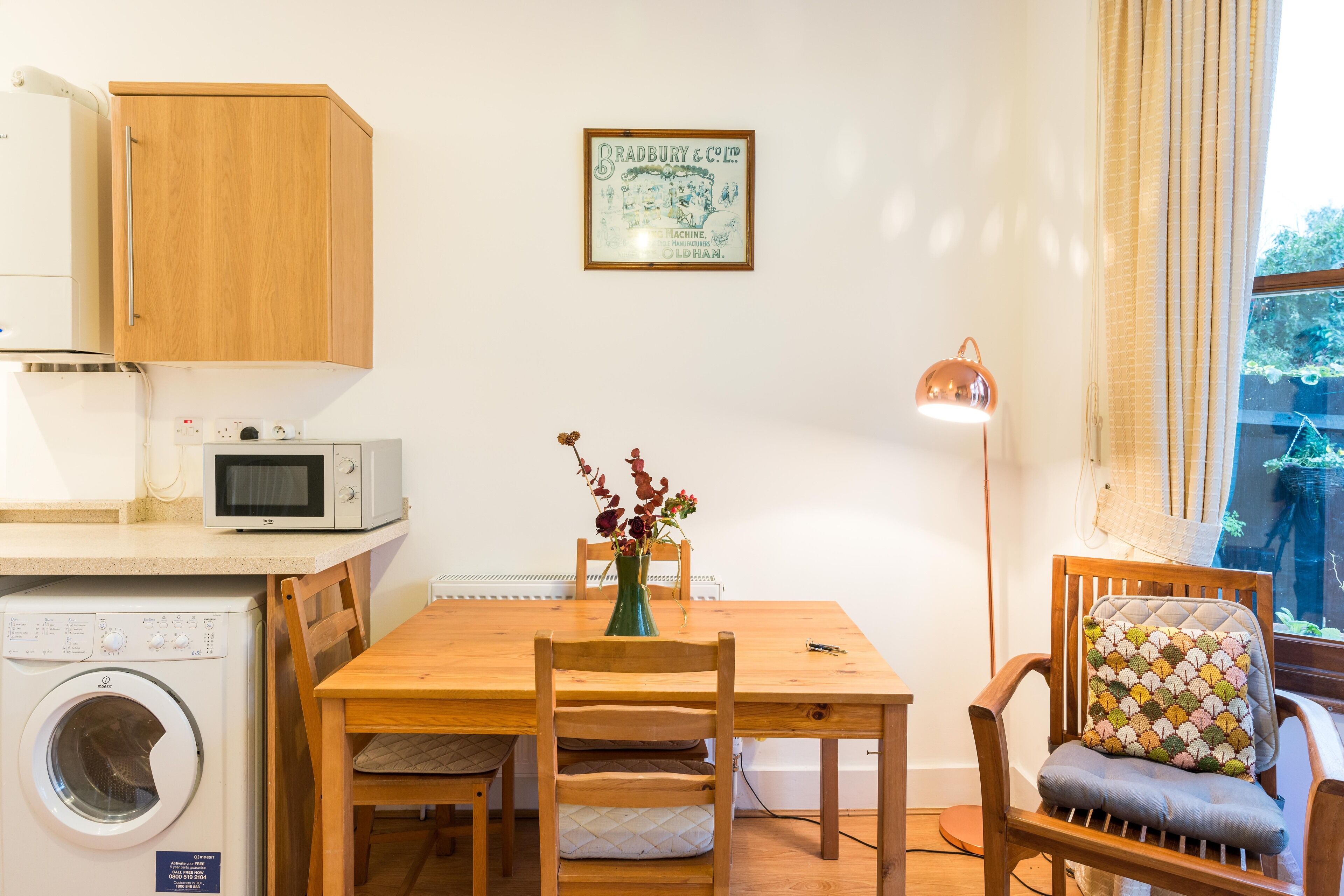 A compact kitchen with a washing machine, a microwave, and a wooden cabinet.