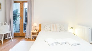 Ein Schlafzimmer mit einem Bett, einem Sessel, einem Nachttisch und einem Fenster mit Vorhängen.