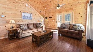 A cozy log cabin interior with two sofas, a wooden coffee table, and a ceiling fan.