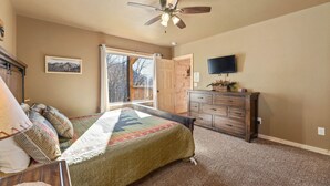 A bedroom with a bed, a dresser, a ceiling fan, a TV, and a window with a view of the outdoors.