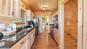 A wooden cabin interior with a kitchen featuring wooden cabinets, a black countertop, and a central island.