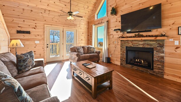 A log cabin interior with a fireplace, a television mounted on the wall, a sofa, and a coffee table.