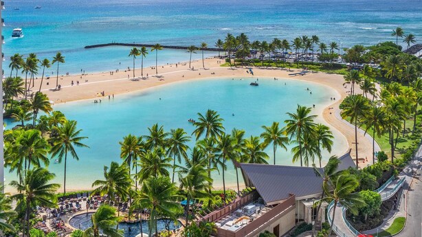 Un resort con una piscina grande, playa y palmeras.