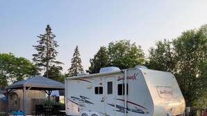 A recreational vehicle with a covered patio area, a small deck, and a fenced yard. - Little Happy Place (Belwood)