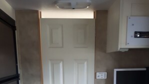 A compact kitchen with a white door, a microwave, and a television on a stand. - Little Happy Place (Belwood)