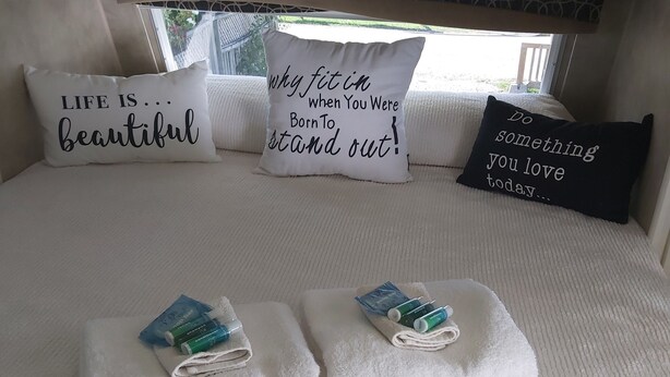 A neatly made bed with towels and toiletries, a window with a view, and motivational pillows. - Little Happy Place (Belwood)