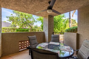 A glass-top table with two chairs, a ceiling fan, and a view of greenery outside. - Regency Resort Luxury Condo (Scottsdale)