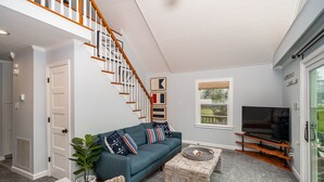 A living room with a staircase, a sofa, a television, and a window.