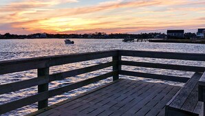 A wooden pier with steps leading into calm water, a boat on the water, and a sunset in the background.