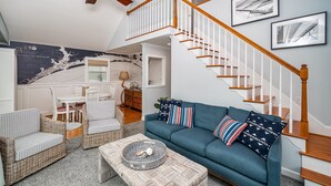 A spacious living room with a blue sofa, wicker chairs, a coffee table, and a staircase with wooden railings.