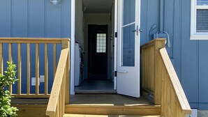 A wooden deck leading to a house with a white door and a small window.