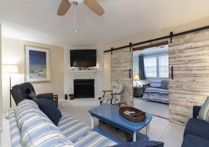 A living room with a sofa, a coffee table, a fireplace, a television, and a sliding door leading to another room.