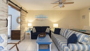 A living room with a sofa, a striped couch, a coffee table, a ceiling fan, and a wall-mounted lamp. - Spacious Townhome ~ Pet Friendly ~ Great Beach Location! (Saint Augustine)