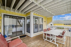 Un espace extérieur abrité, avec une table et des chaises blanches, un mur jaune et une vue sur une maison en arrière-plan.