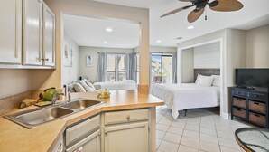 A modern hotel room with a kitchenette, a bed, a TV, and a balcony with a view.