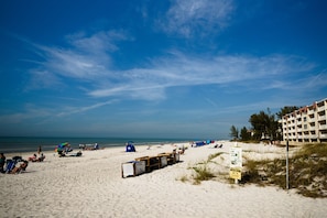 A beach with a sandy shore, umbrellas, and a building in the background.