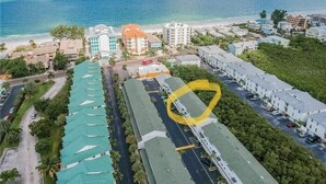 An aerial view of a coastal hotel with multiple buildings, a parking lot, and a view of the ocean. - Beautiful Townhome Steps from Beach (Indian Shores)