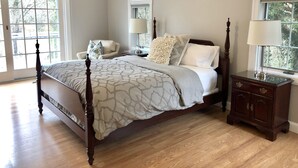 Un dormitorio con cama con dosel, una mesita de noche, una silla y una ventana con vistas a árboles.