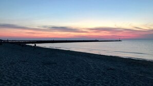 Una playa con un mar tranquilo, un muelle que se adentra en el agua y un cielo al atardecer.