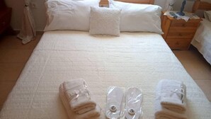 A neatly made bed with white linens, two folded towels, and a pair of slippers on the bed. - Yria suite (Katastari, Allykes)