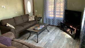 Una sala de estar con sofá, mesa de centro, mueble para televisión y ventana con cortinas.